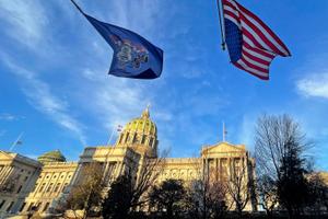 The Pennsylvania and American flags flutter in front of the Capitol building in Harrisburg.